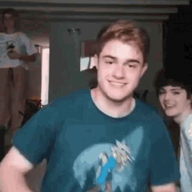 a young man in a blue t-shirt is smiling while standing next to another young man .