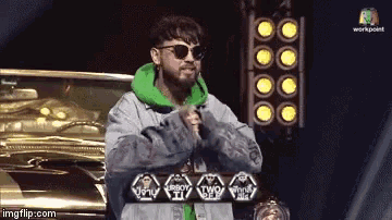 a man wearing sunglasses and a green hoodie is standing in front of a microphone ..