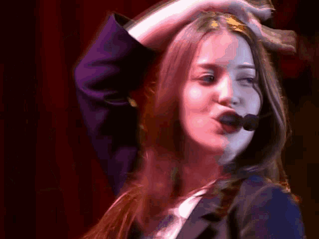 a woman with a microphone in her mouth holds her hand to her hair