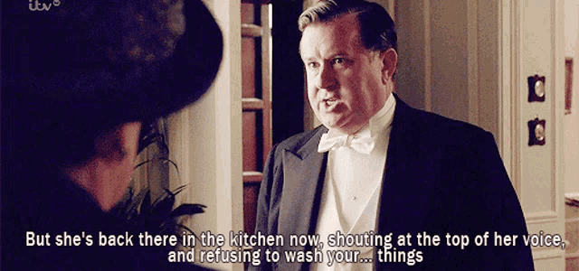 a man in a tuxedo and bow tie is talking to another man in a hat