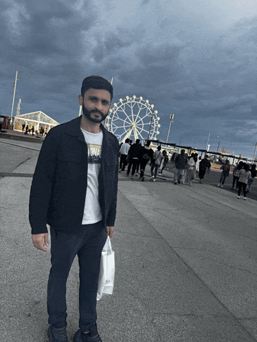 a man stands in front of a ferris wheel with people walking in the background