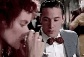 a man in a suit and bow tie is eating a sandwich next to a woman in a bow tie .