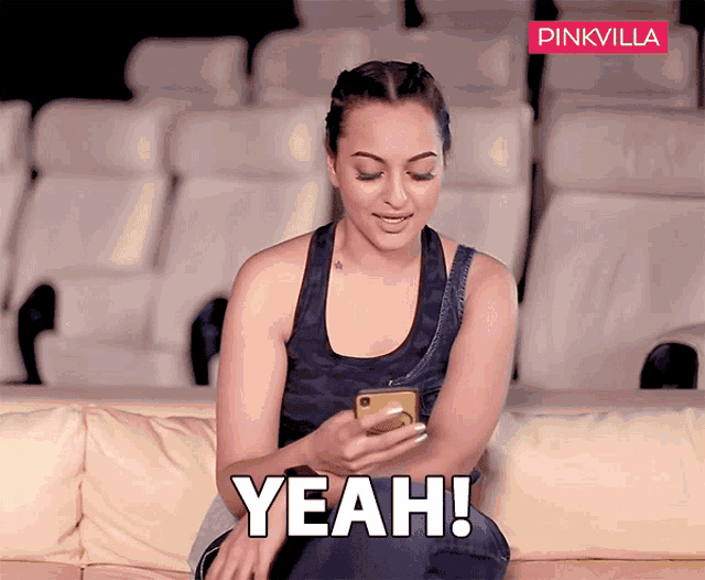 a woman is sitting on a couch looking at her phone and the word yeah is on the screen