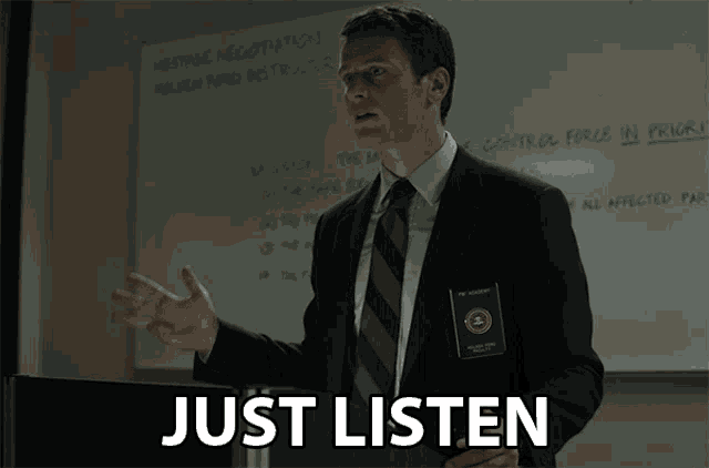 a man in a suit and tie stands in front of a white board with the words just listen on it