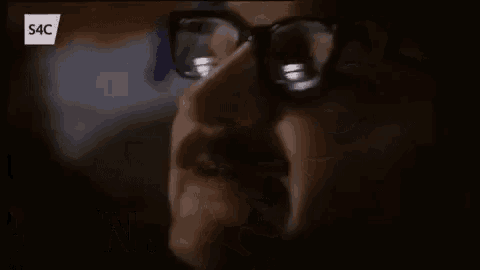 a man wearing glasses and a beard is screaming in a foreign language .