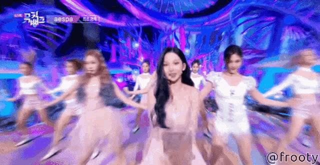 a group of women are dancing on a stage with a woman in a white dress in the foreground .