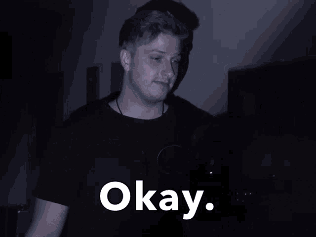 a man in a black shirt is standing in the dark with the word okay written in white