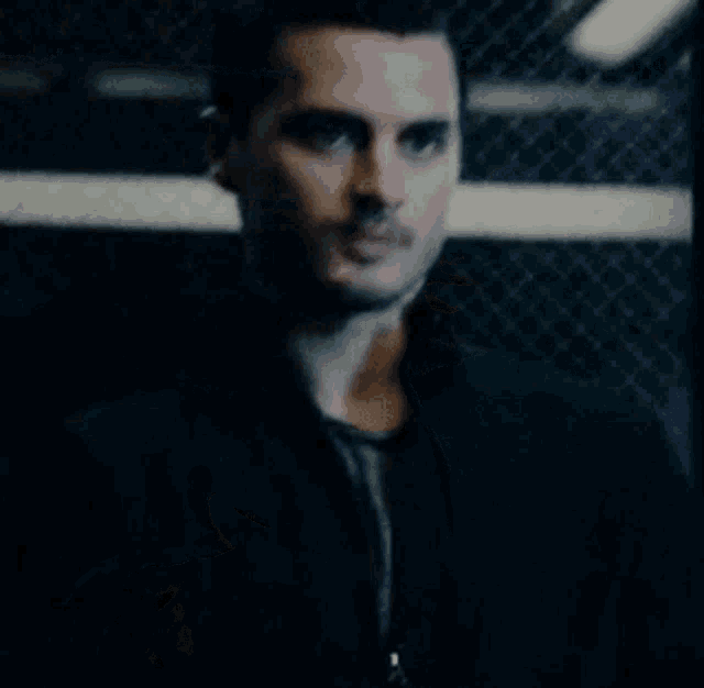 a man in a black jacket is standing in front of a fence