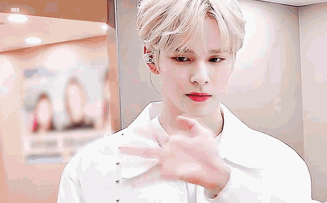 a young man with blonde hair and red lips is wearing a white shirt and a white jacket