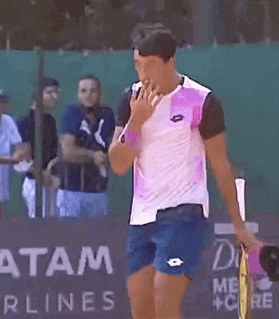 a man in a pink shirt and blue shorts is holding a tennis racquet and talking on a cell phone .
