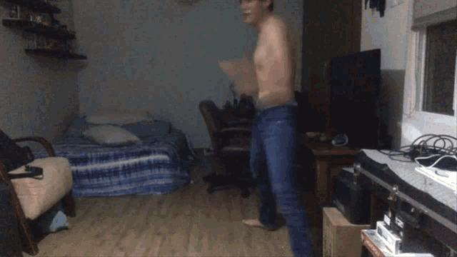 a man without a shirt is dancing in a room with a bed and a tv