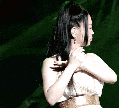 a woman in a white dress with a gold belt holds her hair in a ponytail