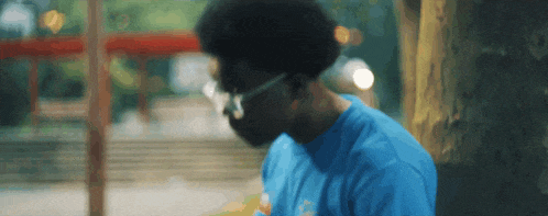 a man wearing glasses and a blue shirt is sitting under a tree in a park .