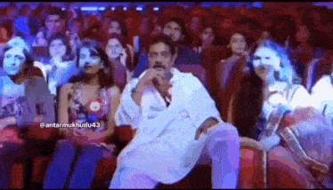 a man in a white shirt is sitting in front of a crowd in a theater .
