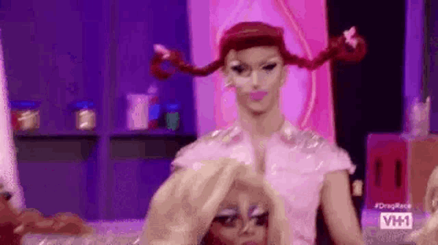 two drag queens are sitting next to each other on a stage . one of the drag queens has pigtails on her head .