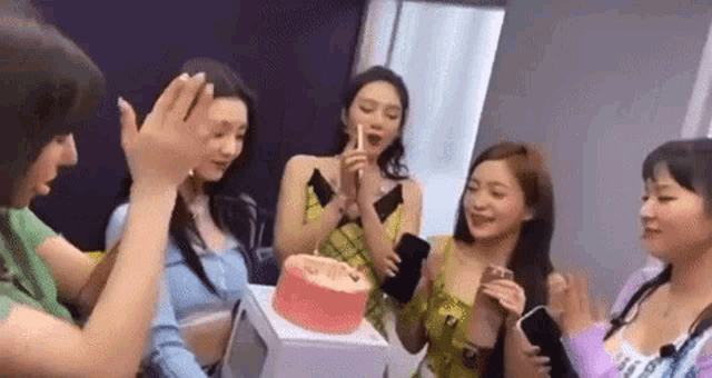 a group of women are celebrating a birthday with a cake in a room .