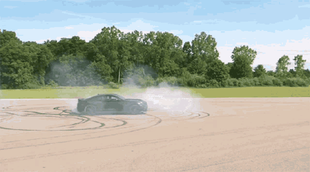a black car is drifting on a dirt road with trees in the background