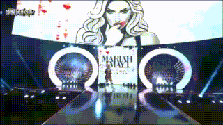 a woman is walking down a runway in front of a sign that says mariah may i
