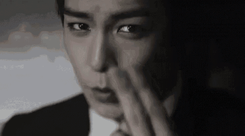 a man in a suit and tie is covering his nose with his hand in a black and white photo .