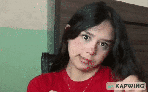 a woman in a red shirt is making a funny face in front of a sign that says kapwing