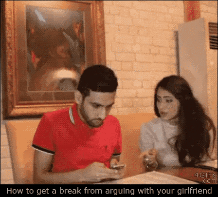 a man in a red shirt is looking at his phone while his girlfriend looks on .