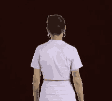 the back of a woman wearing a white shirt and shorts is standing in front of a dark background .