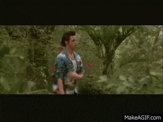 a man in a white tank top is walking through a lush green forest
