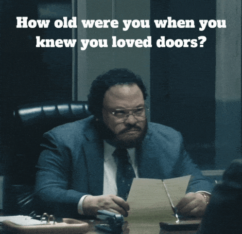 a man in a suit and tie sits at a desk with a question about how old he was when he knew you loved doors