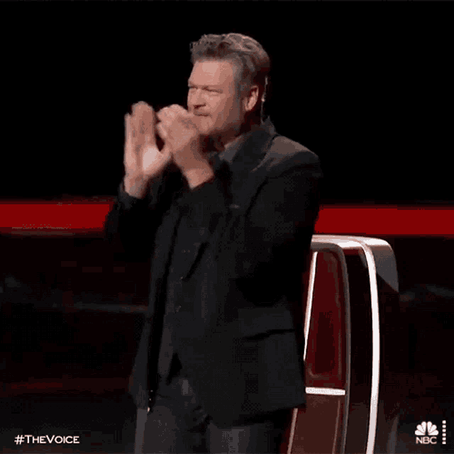 a man in a suit is applauding on a stage while sitting in front of a microphone .