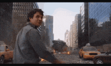 a man is standing in the middle of a city with a taxi cab in the foreground .