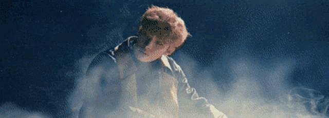 a man with red hair is standing in a cloud of smoke in a dark room .