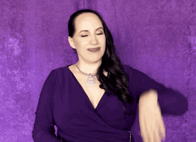 a woman in a purple dress is dancing in front of a purple wall .