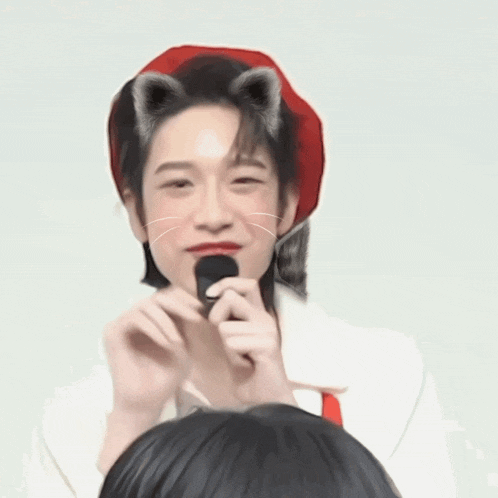 a person wearing a red hat with cat ears is holding a microphone in front of their face