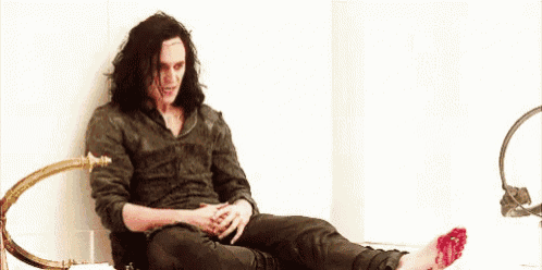 a man with long hair is sitting on a bed with blood on his foot .