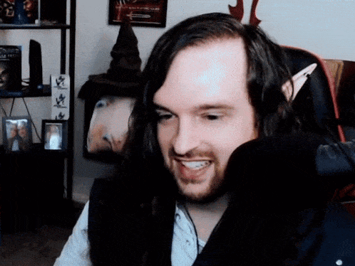 a man with long hair and a beard is smiling in front of a picture of a couple