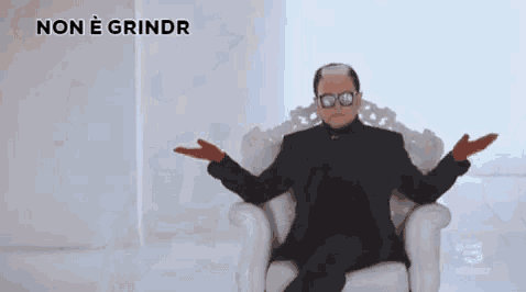 a man in a suit and sunglasses is sitting in a white chair with the words non e grindr written above him