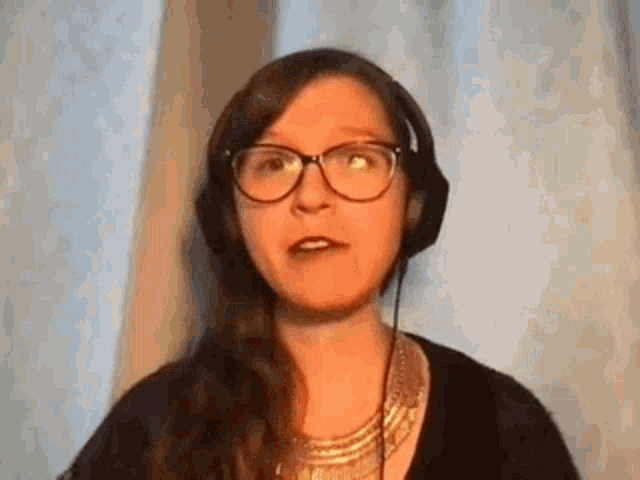 a woman wearing glasses and headphones is standing in front of a window .