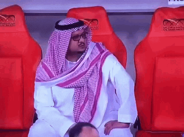 a man in a sheikh 's outfit is sitting in a row of red seats .