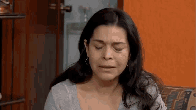 a woman is crying and sitting on a couch with her eyes closed .