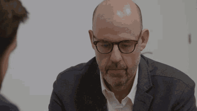 a bald man with glasses and a beard is looking at another man