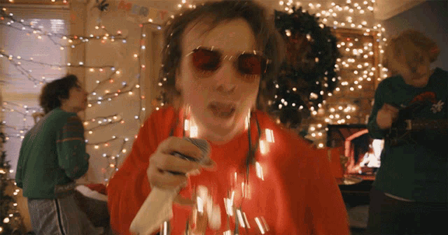 a man singing into a microphone with a merry christmas banner hanging in the background