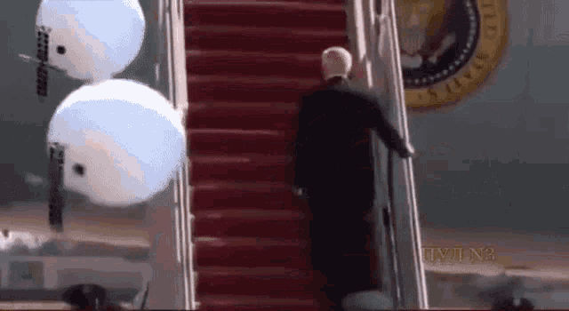 a man in a suit is walking up a set of stairs with a white house seal in the background .