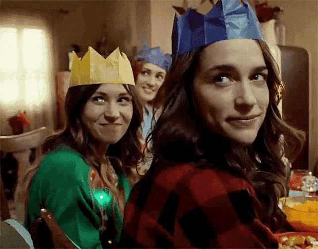 three women wearing paper crowns are sitting at a table with food .