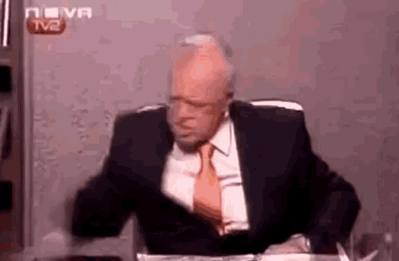 a man in a suit and tie is sitting at a table with his arms outstretched .