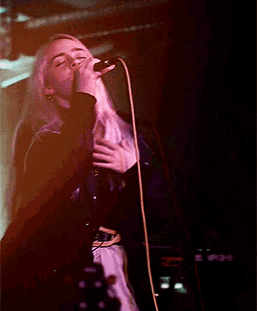 a woman singing into a microphone with her eyes closed in a dark room