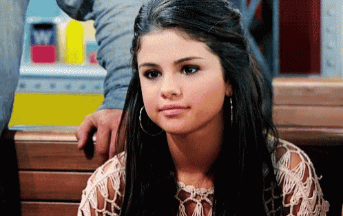 a woman with long black hair and hoop earrings is sitting on a bench