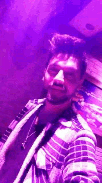 a man is taking a selfie in a dark room with purple lights behind him .