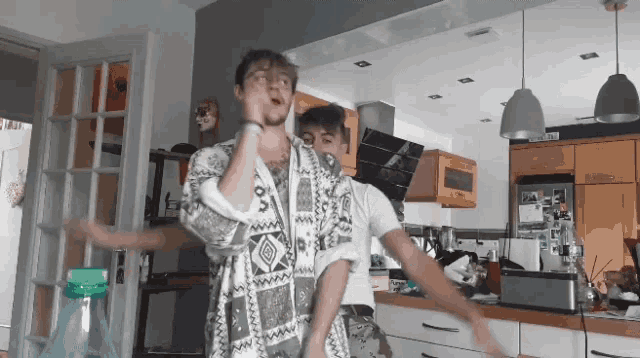 two men dancing in a kitchen with one wearing a shirt that says ' www ' on it