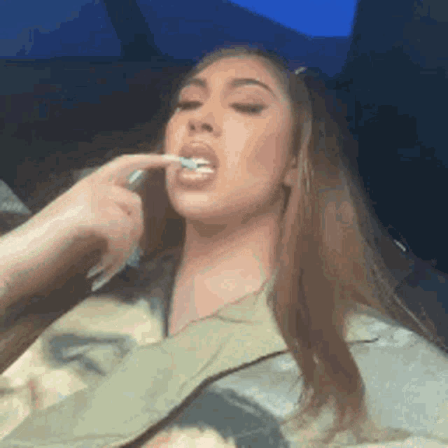 a woman is brushing her teeth in a car while holding a toothbrush in her mouth .