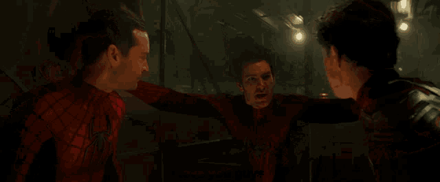 three men in spiderman costumes are talking to each other in a dark room